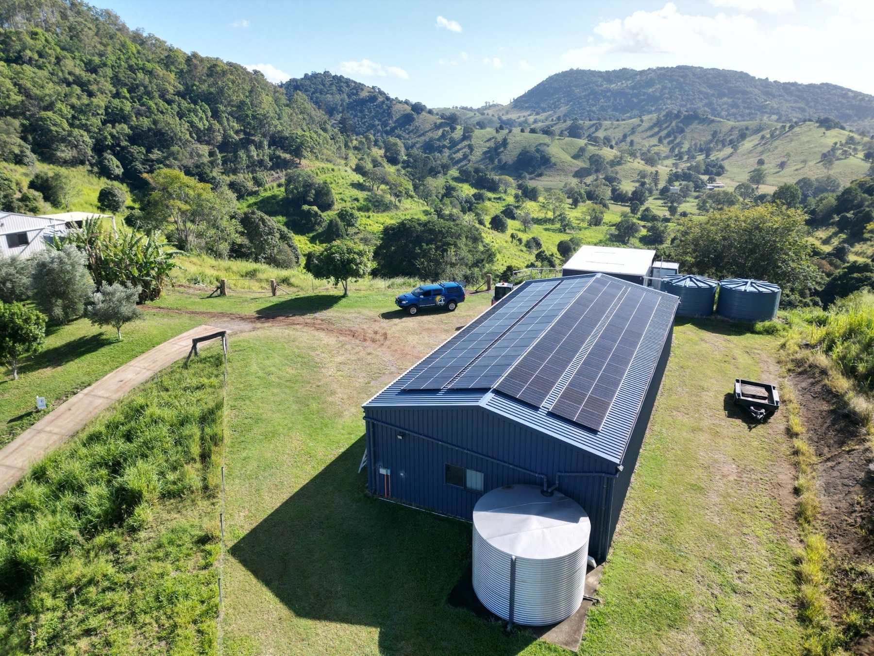 Drone view of an off-grid solar shed with water tanks in the green hills of South East Queensland
